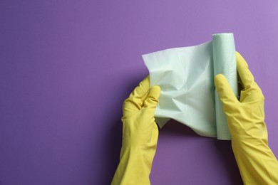 Photo of Janitor in rubber gloves holding roll of color garbage bags over purple background, top view. Space for text