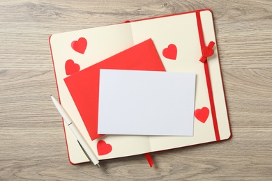 Blank card, envelope and notebook on wooden background, top view with space for text. Valentine's Day celebration