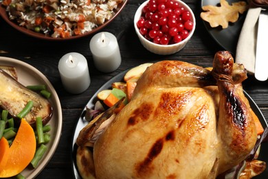Photo of Traditional Thanksgiving day feast with delicious cooked turkey and other seasonal dishes served on black wooden table, closeup