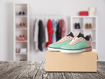 Image of Pair of stylish modern shoes and carton box on wooden surface in store 
