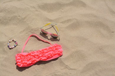 Sunglasses, bra and bracelet on sand, above view with space for text. Beach accessories