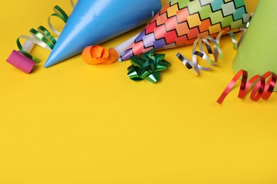 Photo of Party blowers, hats and streamers for birthday party on yellow background. Space for text