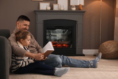 Happy father and daughter reading book together on floor near fireplace at home