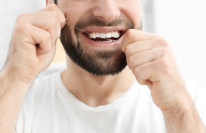 Young man flossing his teeth indoors