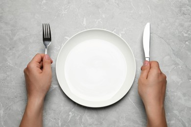 Top view of man with cutlery and empty plate at light grey table, closeup