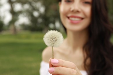 Beautiful young woman holding dandelion outdoors, focus on hand with flower. Allergy free concept
