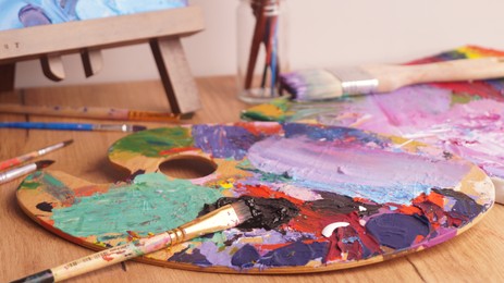 Photo of Artist's palette with mixed bright paints and brush on wooden table