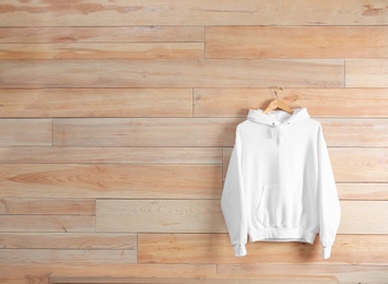 Photo of New hoodie sweater with hanger on wooden wall. Mockup for design