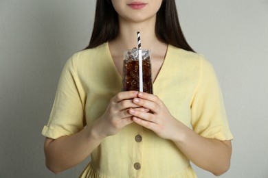 Photo of Woman holding glass of cola with ice and straw on beige background, closeup. Refreshing soda water