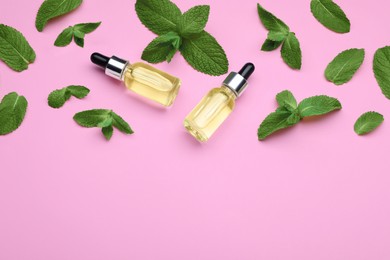 Bottles of essential oil and mint on pink background, flat lay. Space for text