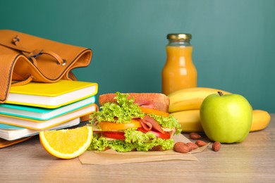 Tasty healthy food and different stationery on wooden table near green chalkboard. School lunch