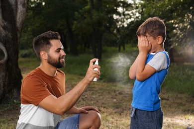 Man applying insect repellent on his son in park. Tick bites prevention