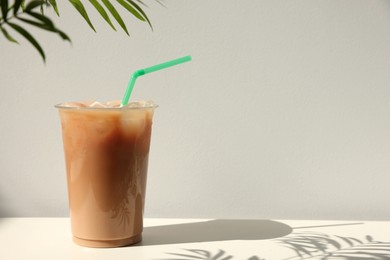 Plastic takeaway cup of delicious iced coffee on white table under sunlight, space for text