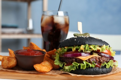 Photo of Board with black burger and french fries on table, closeup