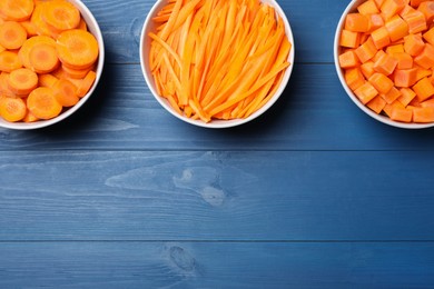 Bowls with cut fresh juicy carrots on blue wooden table, flat lay. Space for text