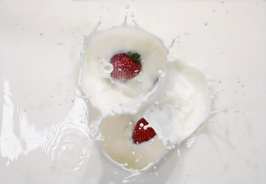 Strawberries falling in milk with splashes, top view