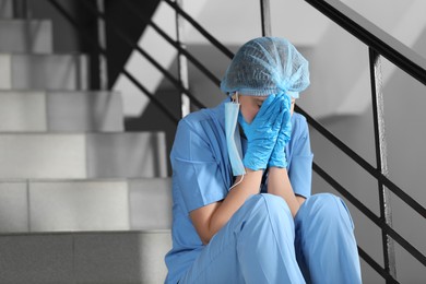 Exhausted doctor sitting on stairs in hospital, space for text