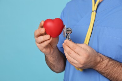 Doctor with stethoscope and red heart on light blue background, closeup. Cardiology concept