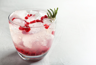 Tasty cocktail with ice cubes and pomegranate on light grey table, closeup. Space for text