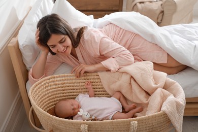Happy young mother resting near cradle with sleeping newborn baby at home