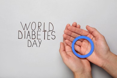 Woman holding blue paper circle near text World Diabetes Day on light background, top view