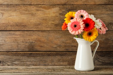 Bouquet of beautiful colorful gerbera flowers in vase on wooden table. Space for text