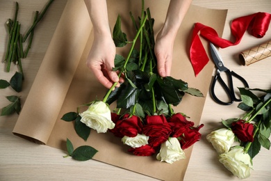 Woman making luxury bouquet of fresh roses at wooden table, top view