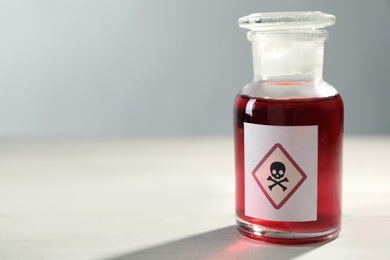 Glass bottle of poison with warning sign on light background, closeup. Space for text