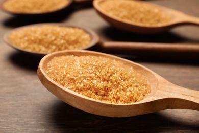 Spoons with brown sugar on wooden table, closeup