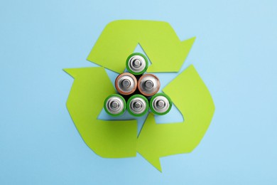 Photo of Used batteries and recycling symbol on light blue background, flat lay
