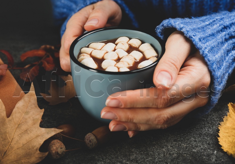 Photo of Woman with cup of hot drink at grey table, closeup. Cozy autumn atmosphere
