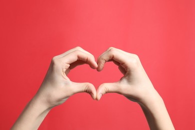 Woman making heart with her hands on red background, closeup