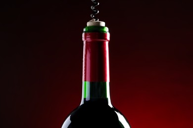 Opening wine bottle with corkscrew on dark red background, closeup