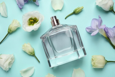 Flat lay composition of bottle with perfume and flowers on cyan background
