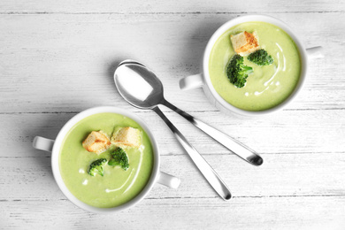 Delicious broccoli cream soup with croutons served on white wooden table, flat lay