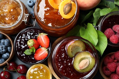 Jars with different jams and fresh fruits on table, flat lay