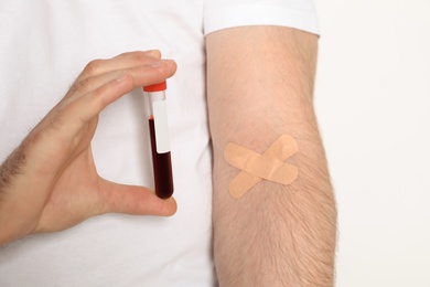 Photo of Man holding test tube near hand with adhesive plasters against white background, closeup. Blood donation concept