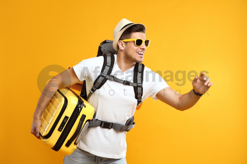 Male tourist with travel backpack and suitcase on yellow background