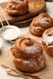 Photo of Delicious profiteroles with powdered sugar on parchment paper, closeup