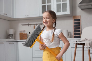 Cute little girl with broom singing while cleaning in kitchen
