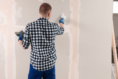 Man plastering wall with putty knife indoors, back view and space for text. Home renovation