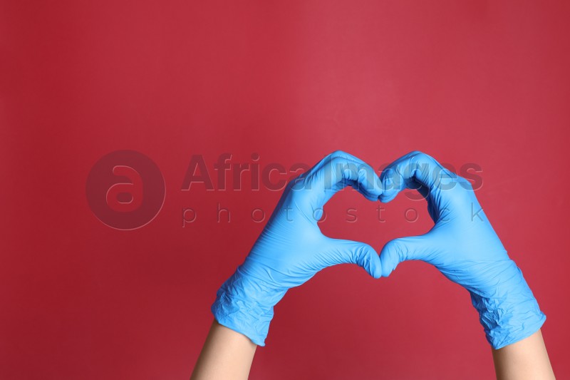 Photo of Doctor in medical gloves making heart with hands on red background, closeup. Space for text