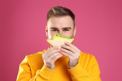 Photo of Young man eating tasty sandwich on pink background
