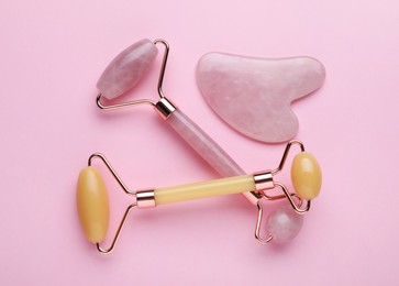 Photo of Gua sha stone and different face rollers on pink background, flat lay