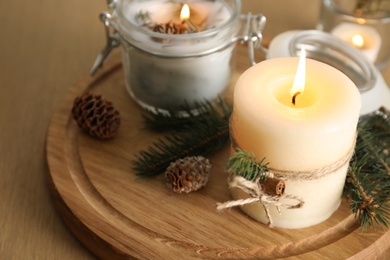 Burning scented conifer candles and Christmas decor on wooden table, closeup