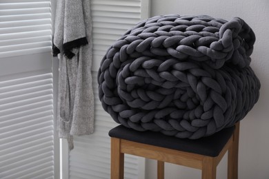 Dark grey chunky knit blanket rolled on wooden stool in room