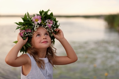 Cute little girl wearing wreath made of beautiful flowers near river