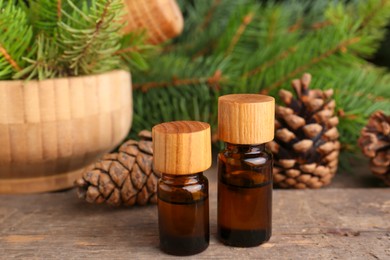 Bottles of pine essential oil, conifer tree branches and cones on wooden table, closeup