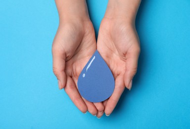 Photo of Save Water concept. Woman holding paper drop on light blue background, top view