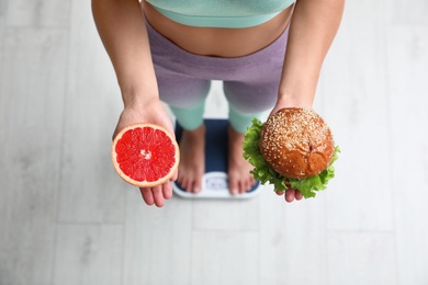 Choice concept. Top view of woman with grapefruit and burger standing on scales, closeup